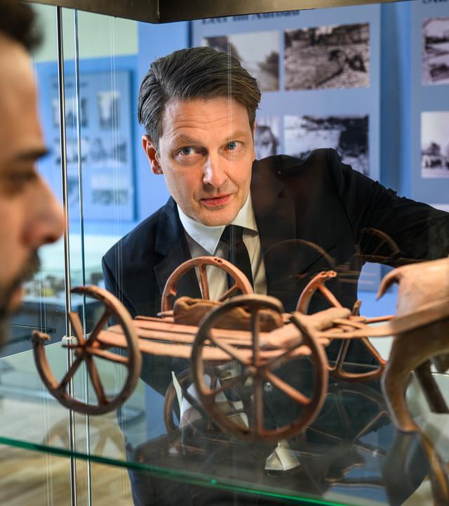 Yunus Özlügül (Yunus Cumartpay) und Wolfgang Habedank (Holger Stockhaus) betrachten konzentriert ein Ausstellungsstück in einer Vitrine, das wie ein antiker Wagen mit Rädern und einer Tierfigur aussieht