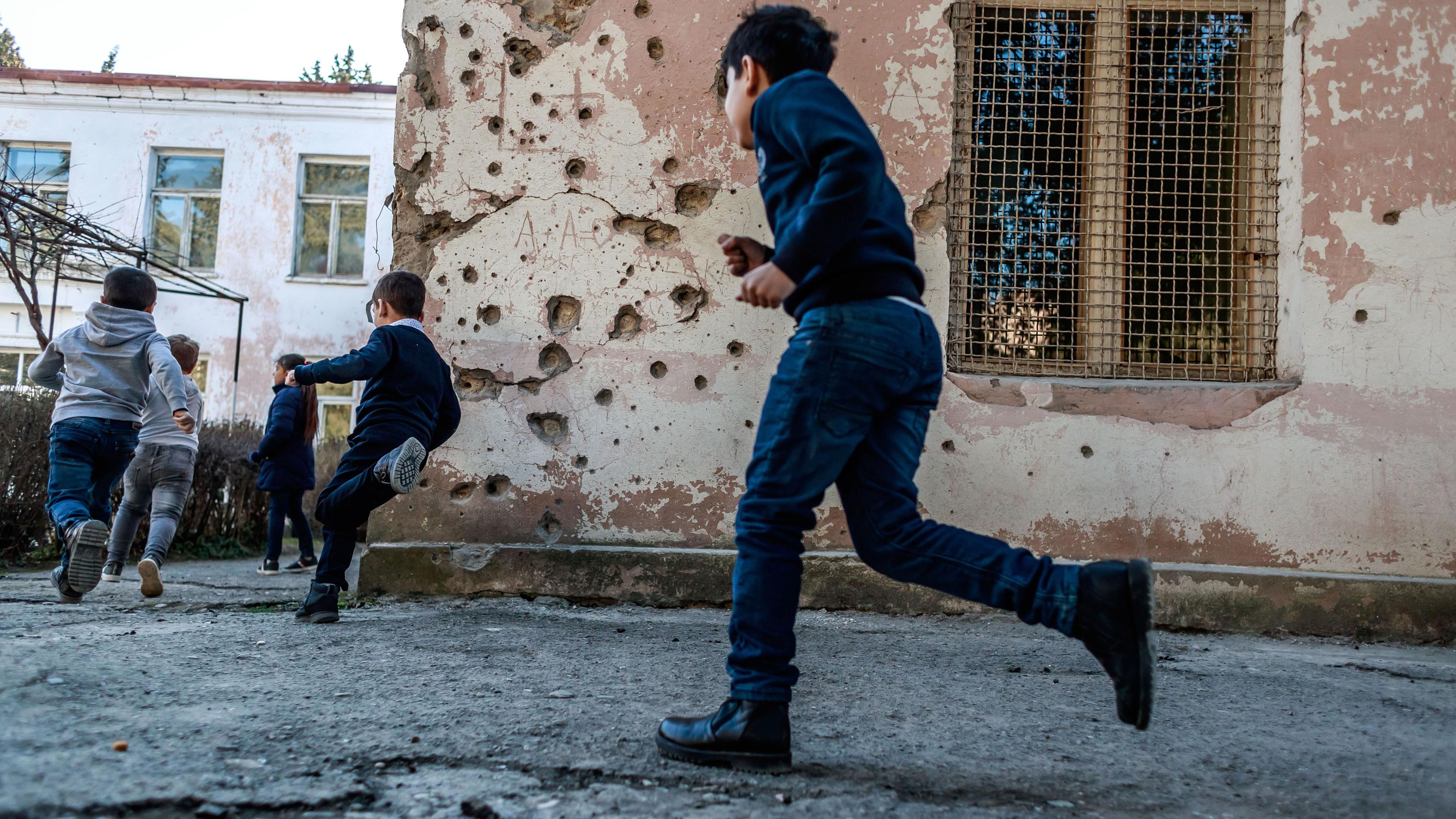 Kinder spielem in nach gewaltsamen Auseinandersetzungen zerstörtem Schulhof in Bergkarabach