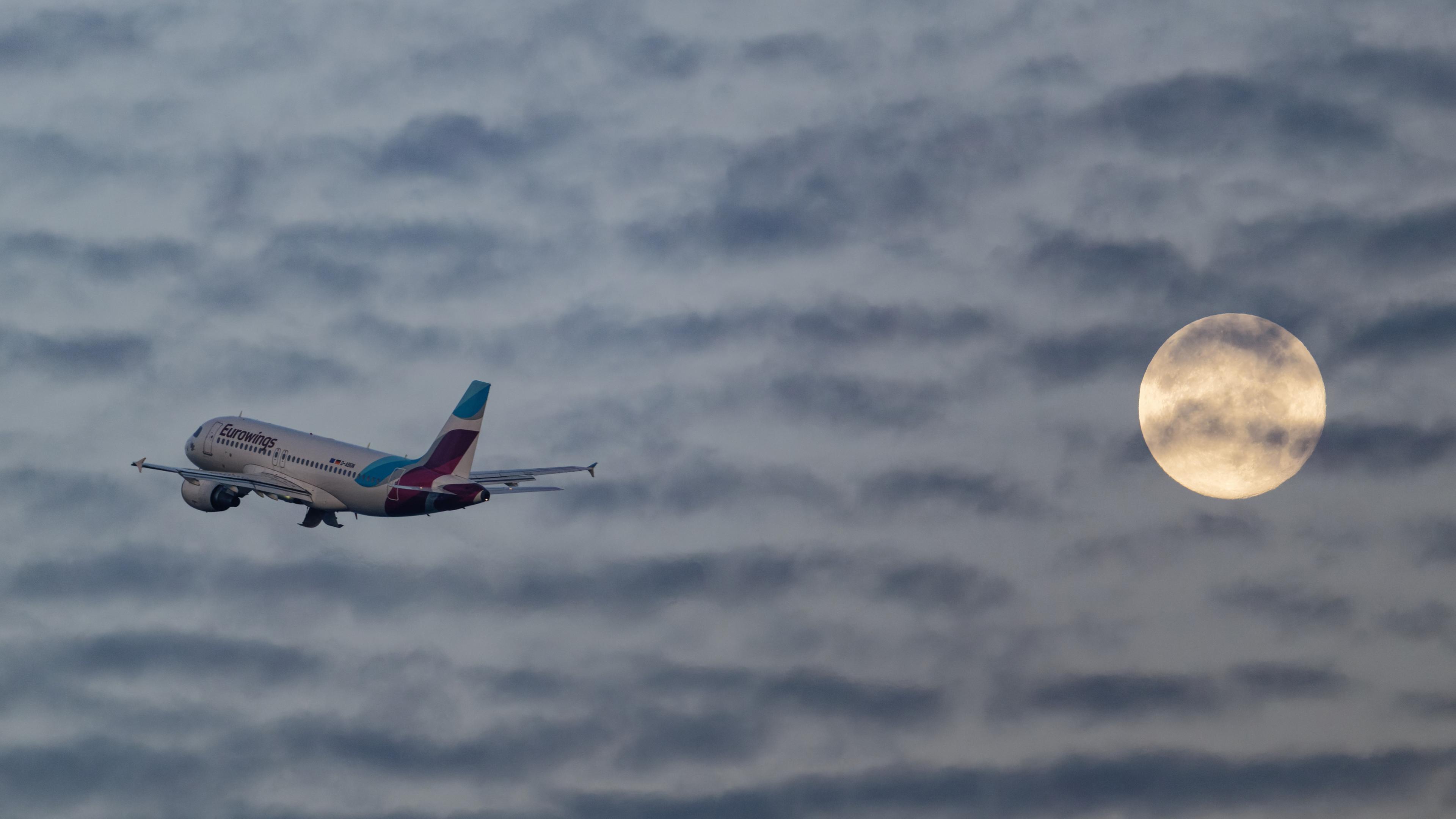 Ein Passagierflugzeug startet vom Flughafen in Düsseldorf, und passiert den Vollmond.