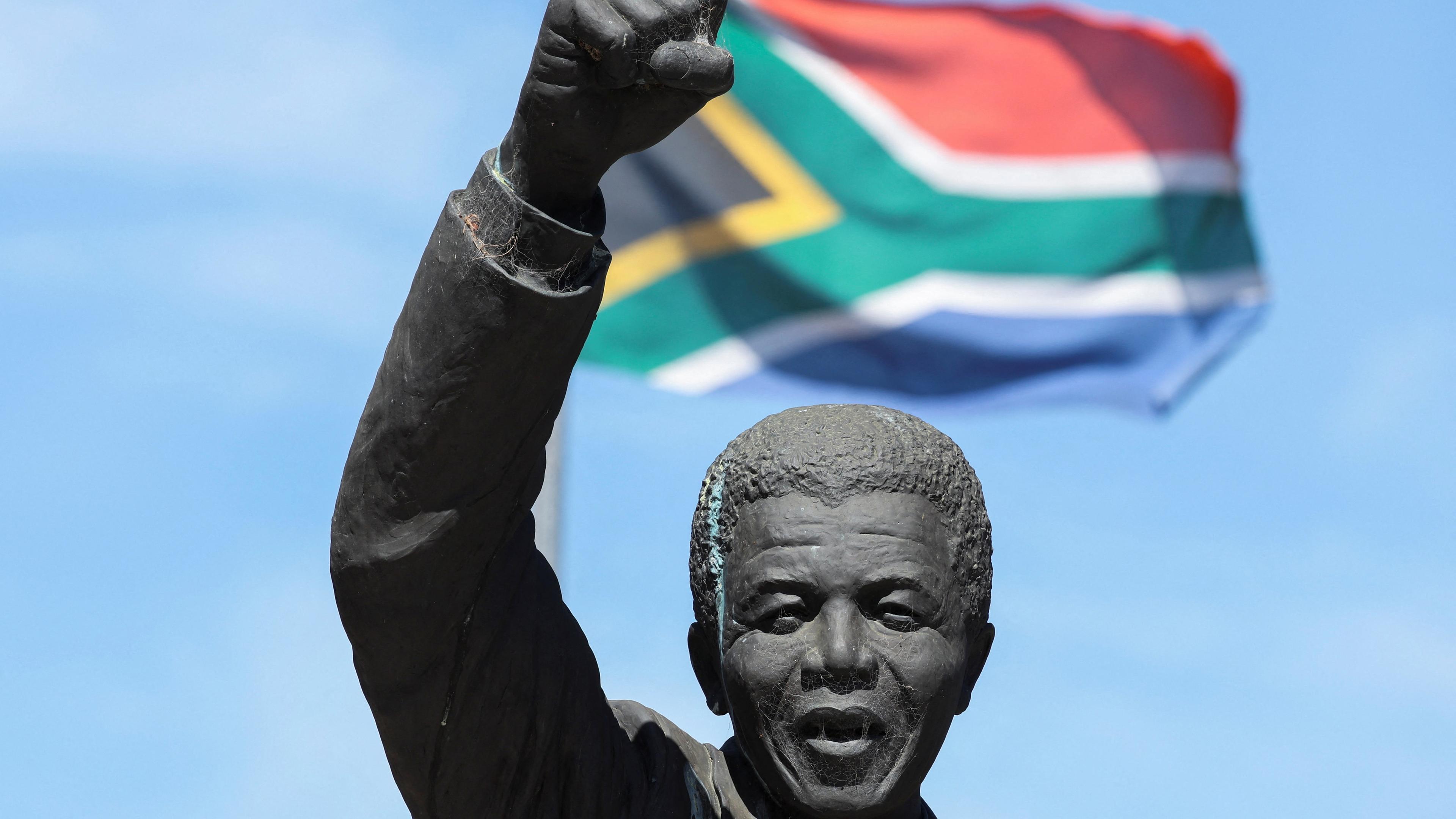 Eine Statue von Nelson Mandela mit hochgerecktem Arm vor einer Südafrika-Flagge.