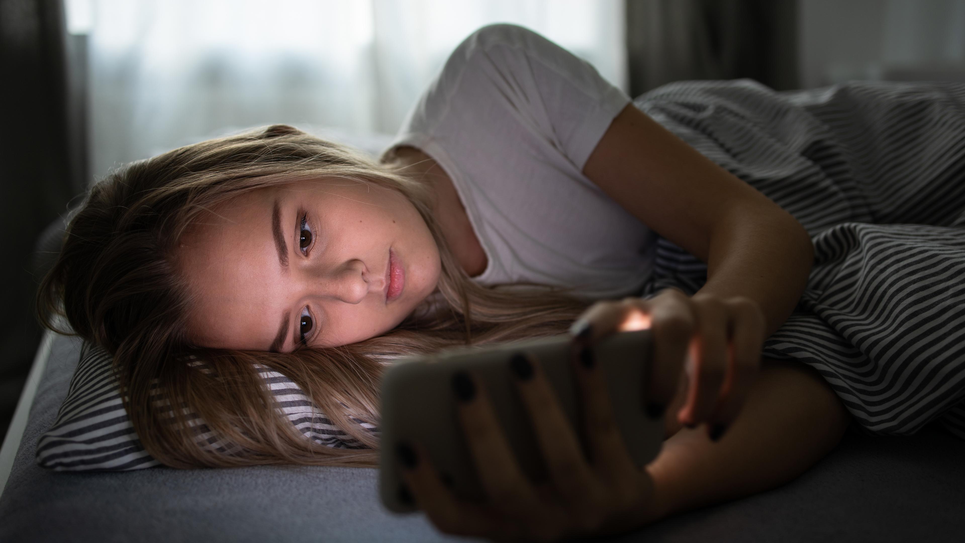 Mädchen liegt mit Smartphone im Bett