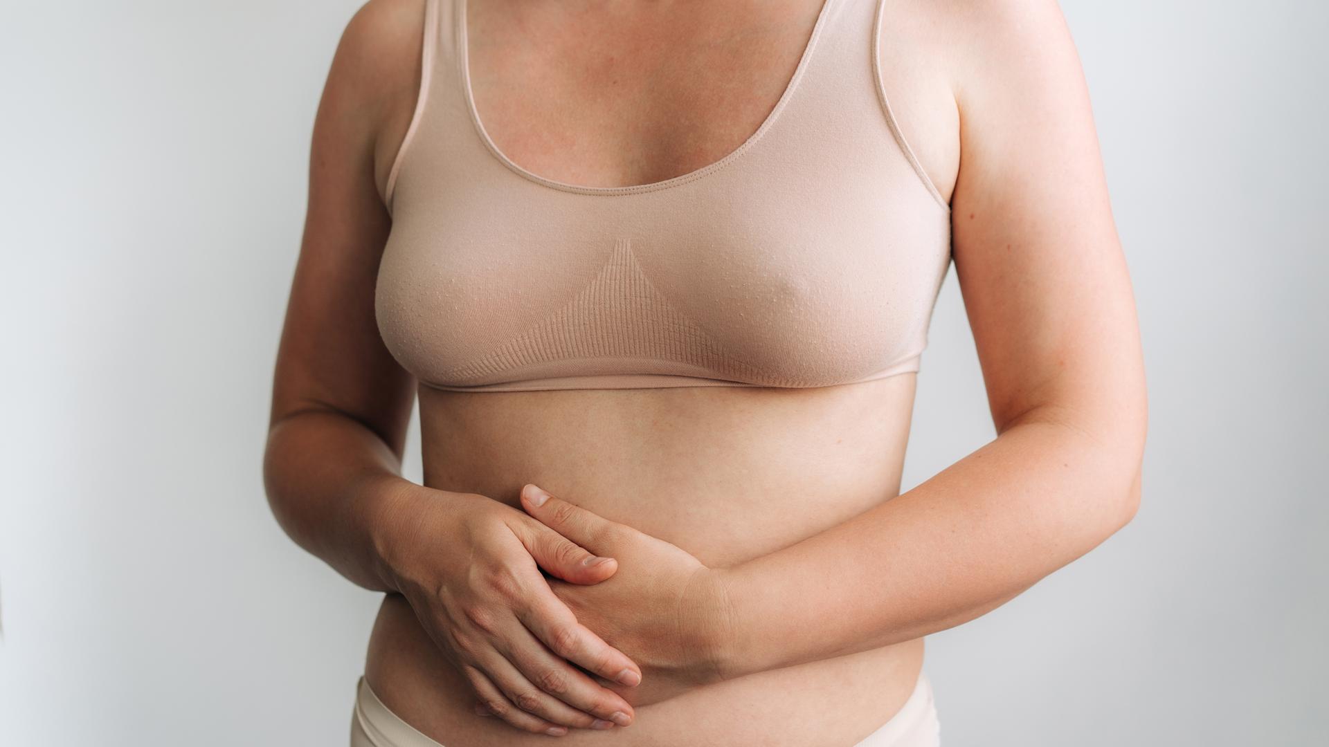 Frau in beige BH hält ihren Magen, Gesundheit und Wellness-Porträt betont Körpervertrauen.