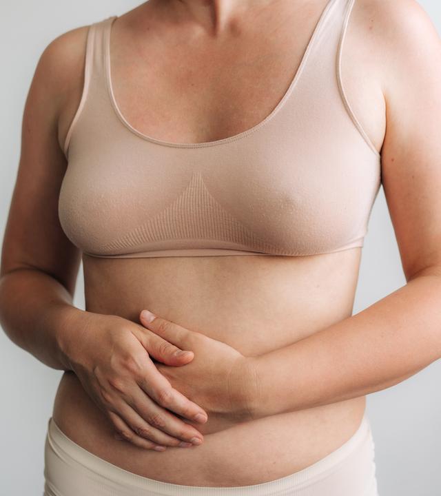 Frau in beige BH hält ihren Magen, Gesundheit und Wellness-Porträt betont Körpervertrauen.