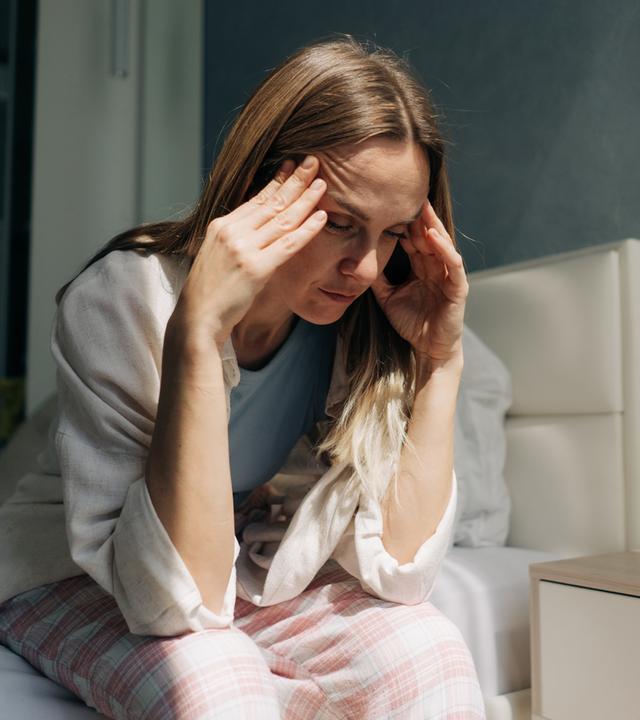 Eine Frau mittleren Alters sitzt zu Hause und hält sich die Hände an die Schläfen. Kopfschmerzen, Frauengesundheit, Hormonspiege