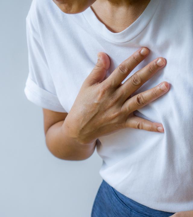 Frau hält sich vornübergebeugt Hand auf die Brust- Symbolbild Asthma