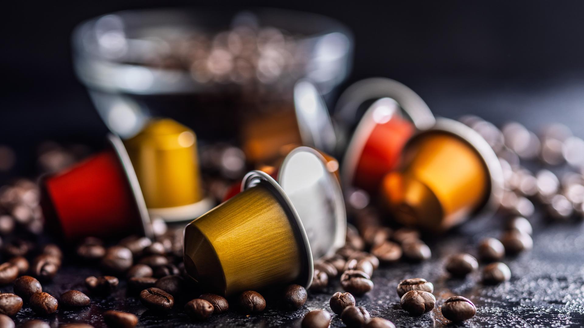Colorful Coffee Capsules and Espresso Pods Scattered Among Roast Coffee Beans on Dark Surface