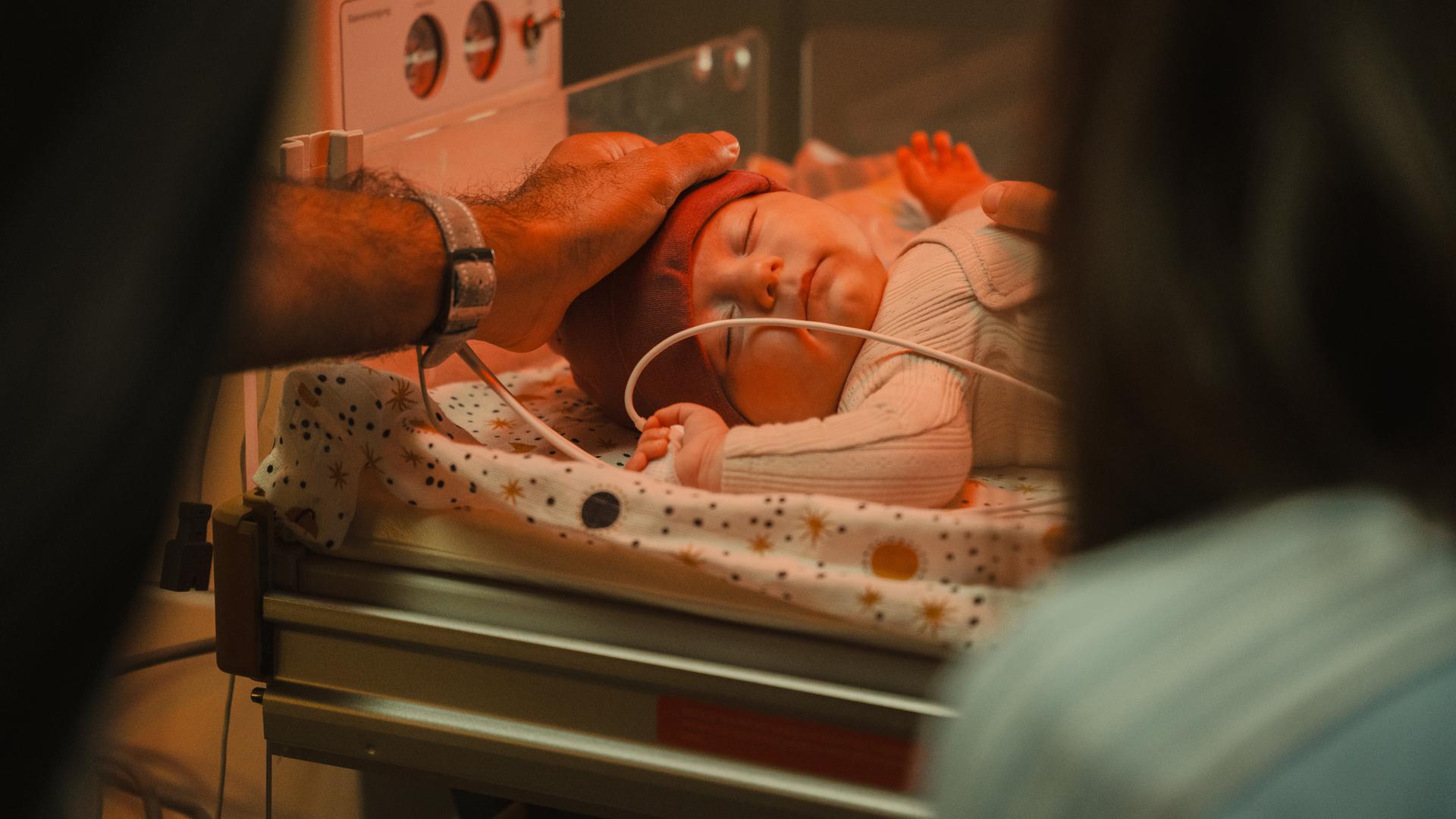 "PUSH - Urvertrauen": Ida (Johanna Reinders) und ihr Freund Giovanni (Hassan Kello) berühren vorsichtig ihr Baby, das in der Klinik auf einem Babybett liegt. Idas Hand liegt auf seinem Bauch, Giovannis Hand auf seinem Kopf.