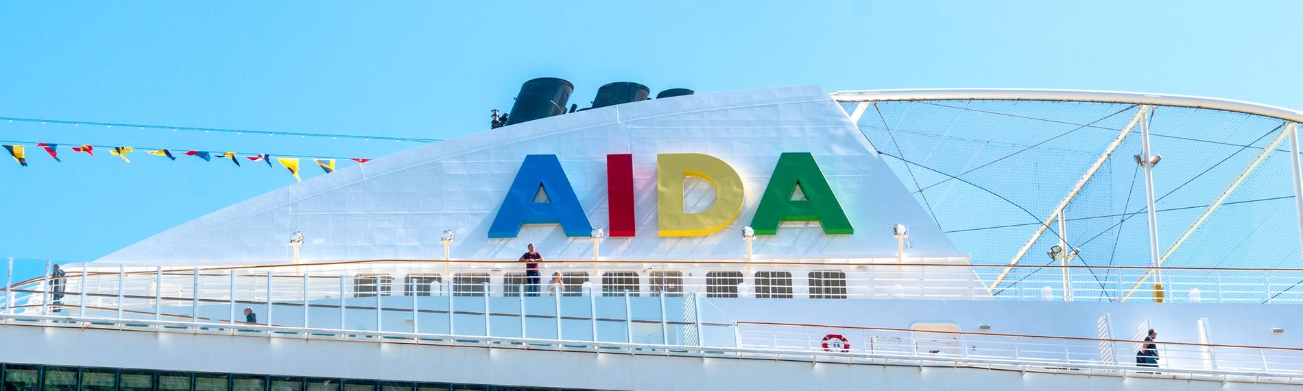Das "AIDA"-Logo ist auf einem Schiffsdach vor blauem Himmel zu sehen.