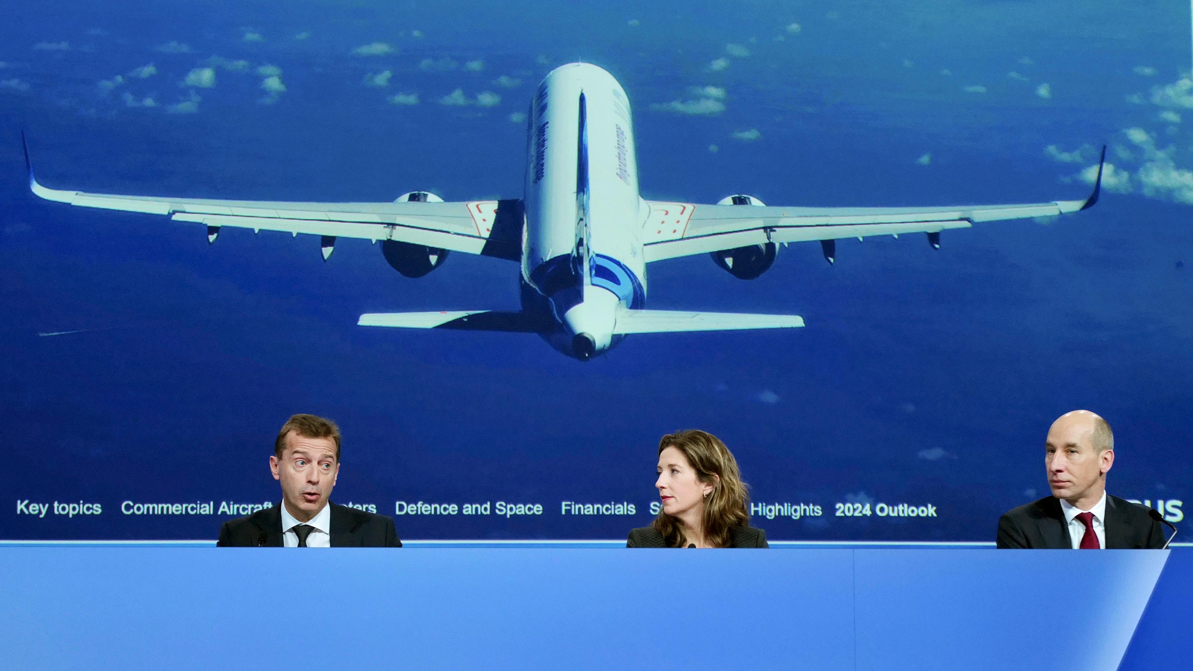 Drei Airbus-Chefs präsentieren die Jahreszahlen. Hinter ihnen ist auf einem Bild ein großes Flugzeug zu sehen. 
