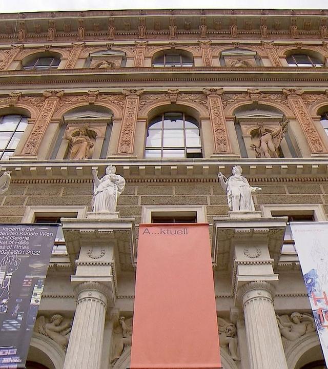 Das Bild zeigt die Fassade der Akademie der bildenden Künste in Wien. Es handelt sich um ein imposantes Gebäude mit mehreren Stockwerken, das von Säulen und Statuen geschmückt ist. Die Statuen sind auf Balustraden platziert und befinden sich auf beiden Seiten des Eingangsbereichs.   Die Fassade weist aufwendig gestaltete Elemente wie Fenster, Verzierungen und Reliefs auf, die das architektonische Gesamtbild prägen. Es sind mehrere Banner angebracht, die Informationen über aktuelle Ausstellungen enthalten.   Der Himmel ist bewölkt, was dem Szenario eine gedämpfte Atmosphäre verleiht. Die Akademie gilt als eine der ältesten Kunstakademien in Europa und hat zahlreiche berühmte Künstler hervorgebracht.