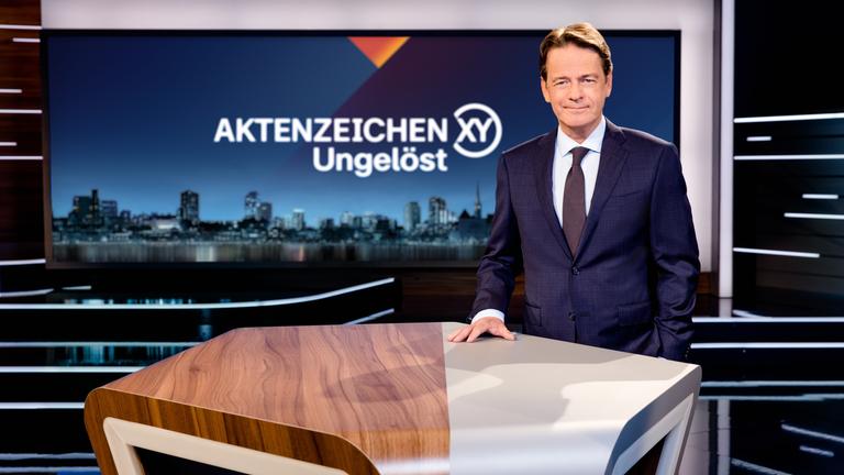 Aktenzeichen XY... Ungelöst": Moderator Rudi Cerne steht im Studio und lächelt in die Kamera.