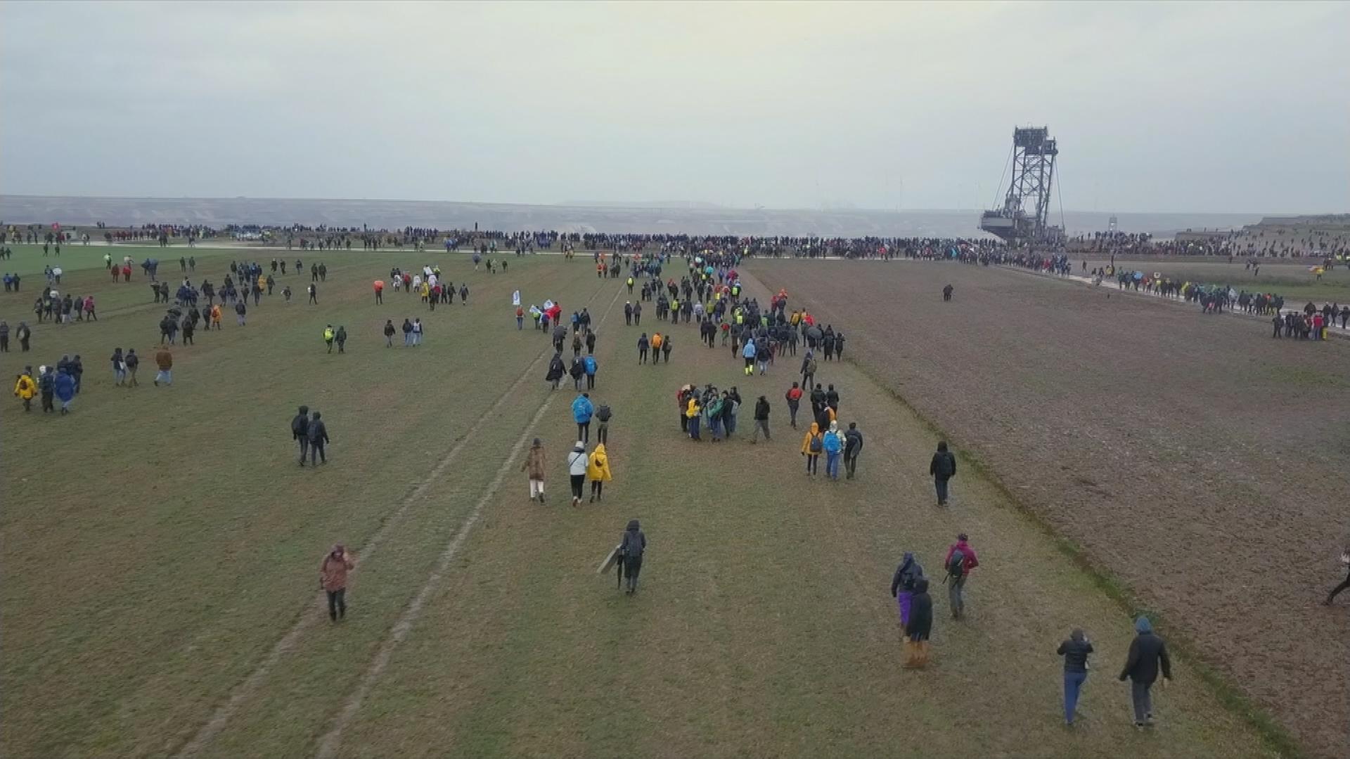 Auf dem Bild sind Klimaaktivisten und Aktivistinnen zu sehen, welche auf die Kante eines Braunkohleabbaugebietes zulaufen um sich dort zu versammeln.