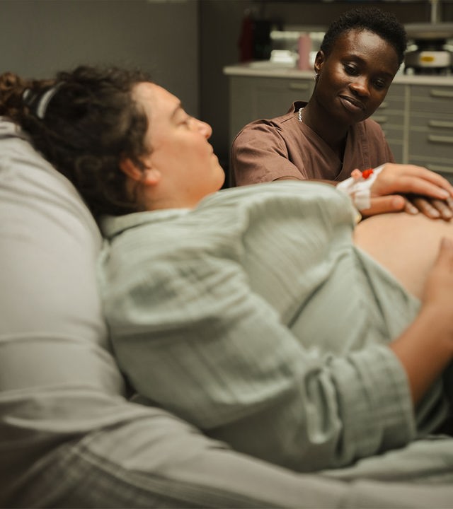 "PUSH - Akzeptanz": Sibel (Nuriye Jendroßek) liegt im Patientenbett und schaut zu Tara (Lorna Ishema), die an ihrem Bett sitzt und eine Hand auf Sibels Babybauch legt. Sibel hält Taras Hand.