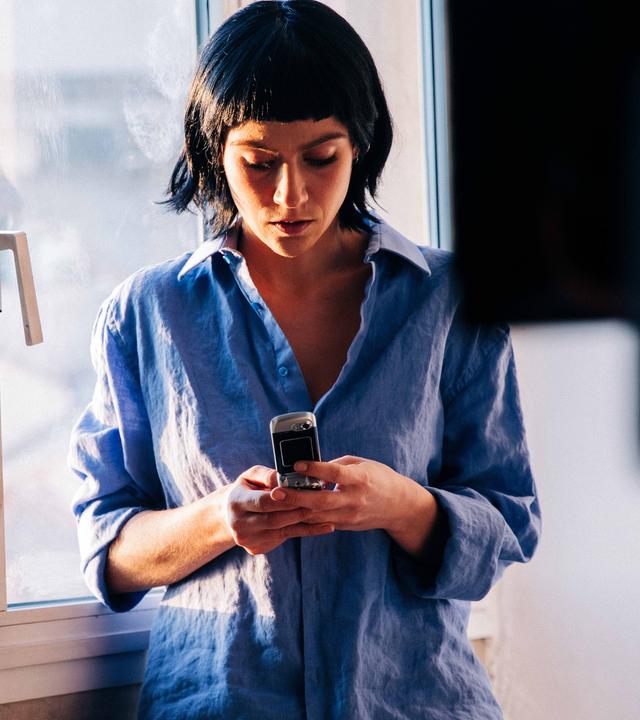 "Survivors": Alex (Sophie Pfennigstorf) steht in ihrer Wohnung vor einer Fensterfront und liest eine Nachricht auf ihrem Handy.