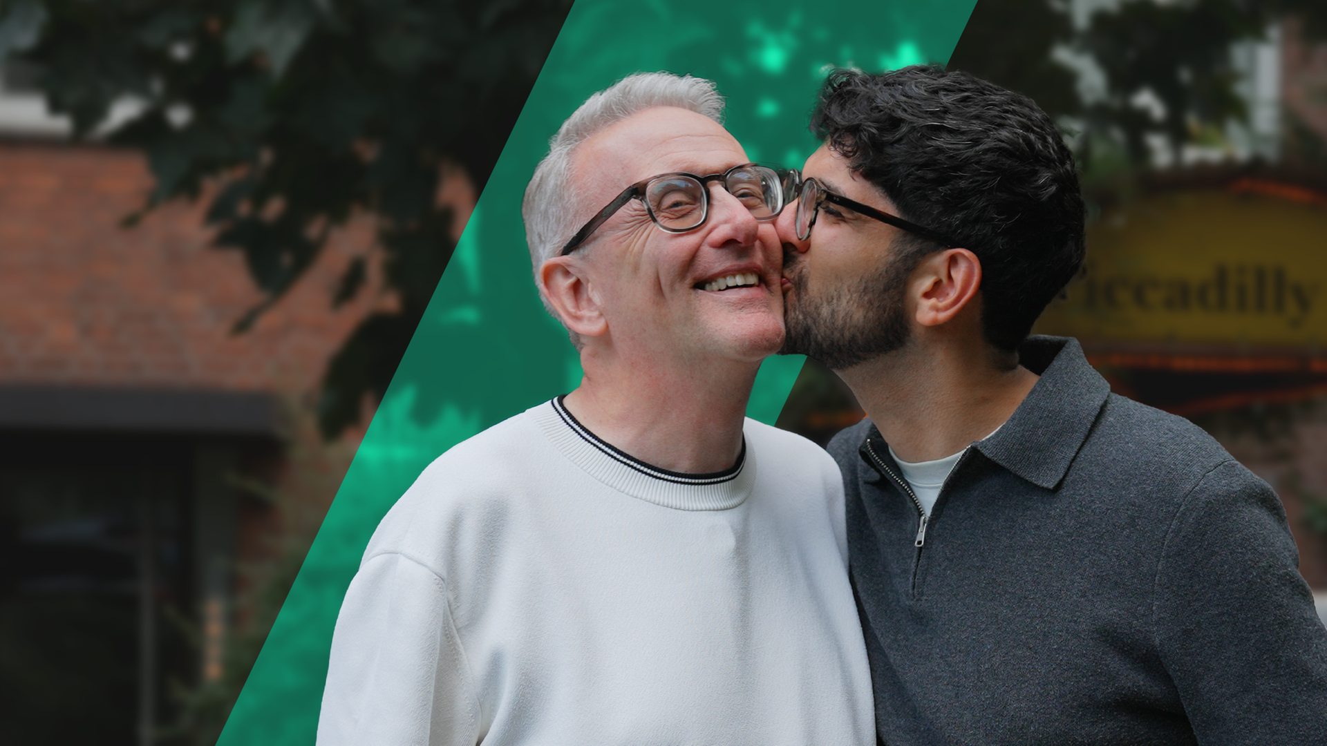 Ali und Markus stehen nebeneinander und Ali gibt Markus ein Küsschen auf die Backe. 