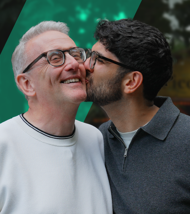 Ali und Markus stehen nebeneinander und Ali gibt Markus ein Küsschen auf die Backe. 