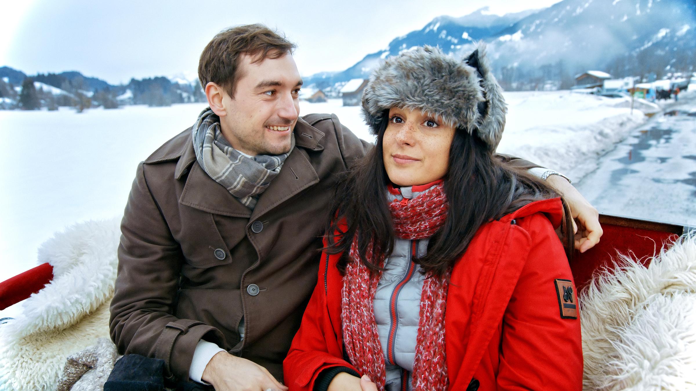 Nicolas (Daniel Gawlowski) und eine Alice (Aybi Era) sitzen in einem Schlitte auf Schaffellen.