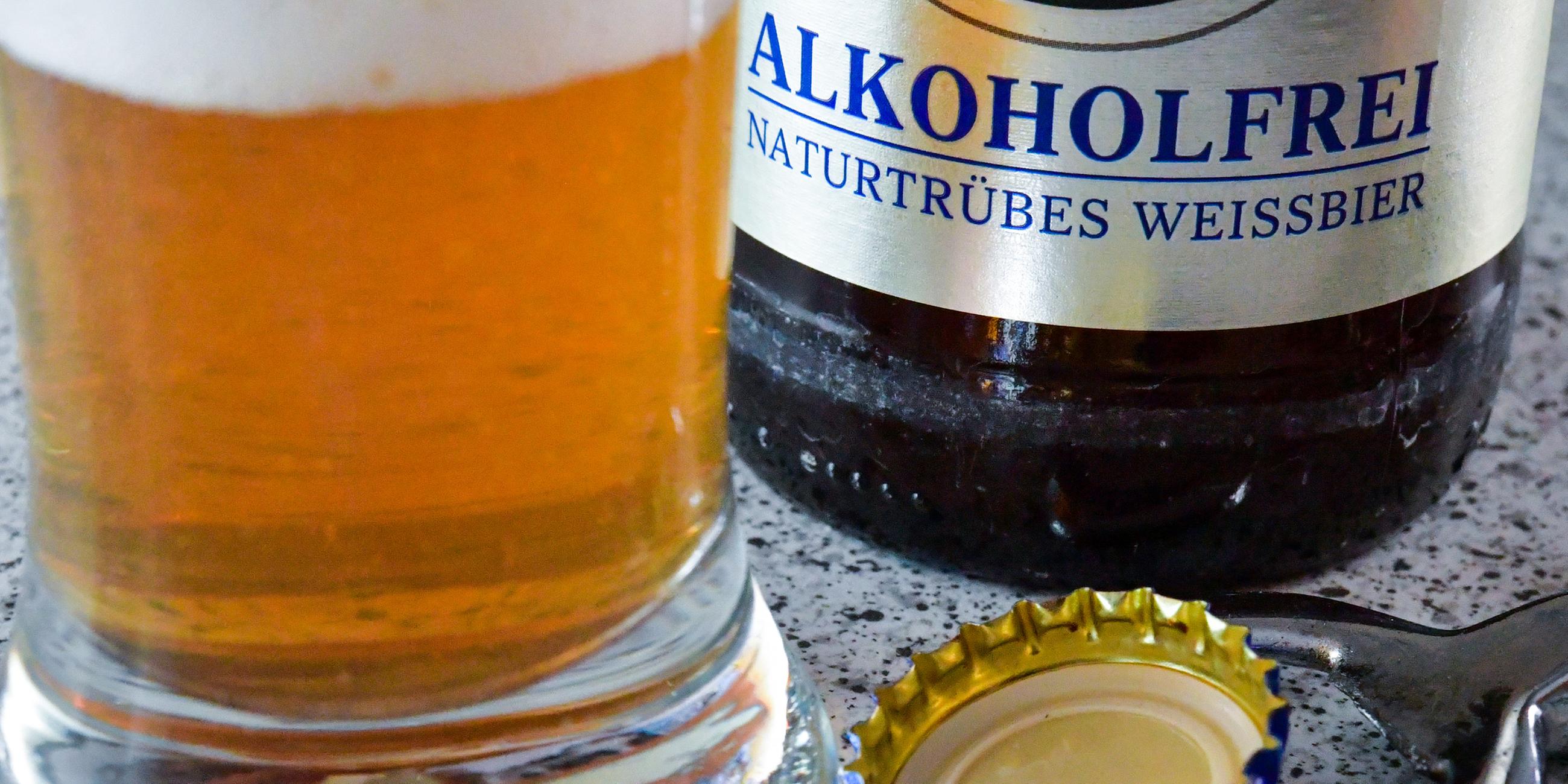 Alkoholfreies Bier in einem Glas neben einer Flasche mit der Aufschrift "Alkoholfrei - naturtrübes Weissbier"