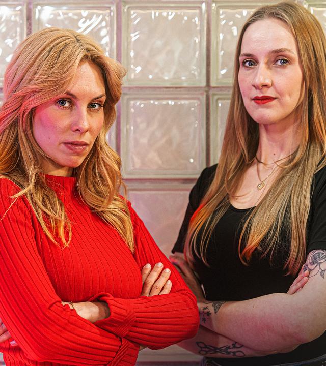 Zwei junge Frauen stehen mit verschränkten Armen und ernstem Blick vor einer Wand.