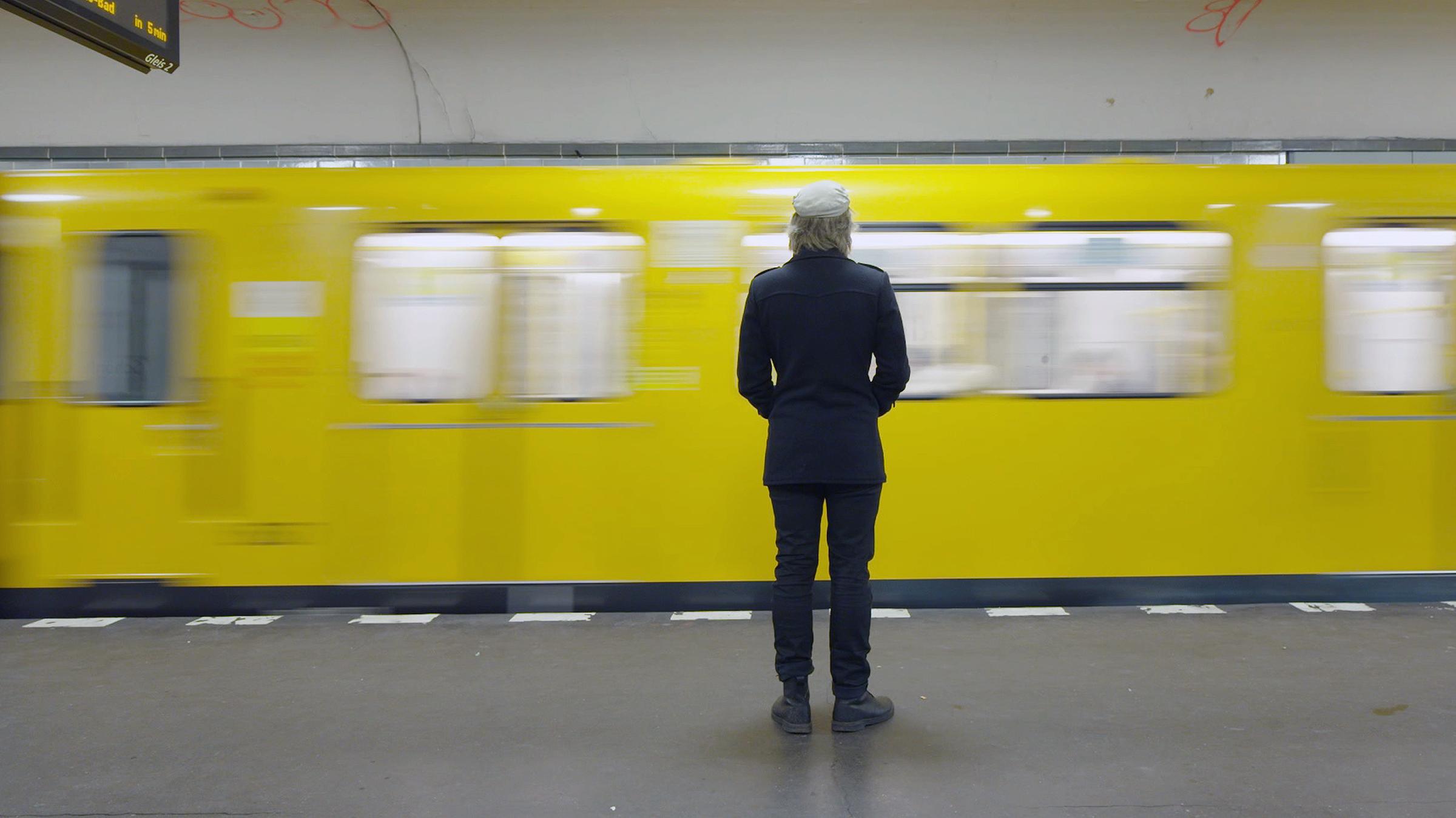 "ZDFzeit: Allein unter Millionen - Die Epidemie der Einsamkeit": Ein Mann steht alleine in einem U-Bahnhof. Vor ihm fährt gerade eine U-Bahn mit gelben Wagons vorbei.