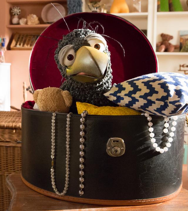 Rudi hockt in seiner Hutschachtel und schaut neugierig in den Laden hinüber. Neben ihm steht ein aufgebautes Brett-Spiel.