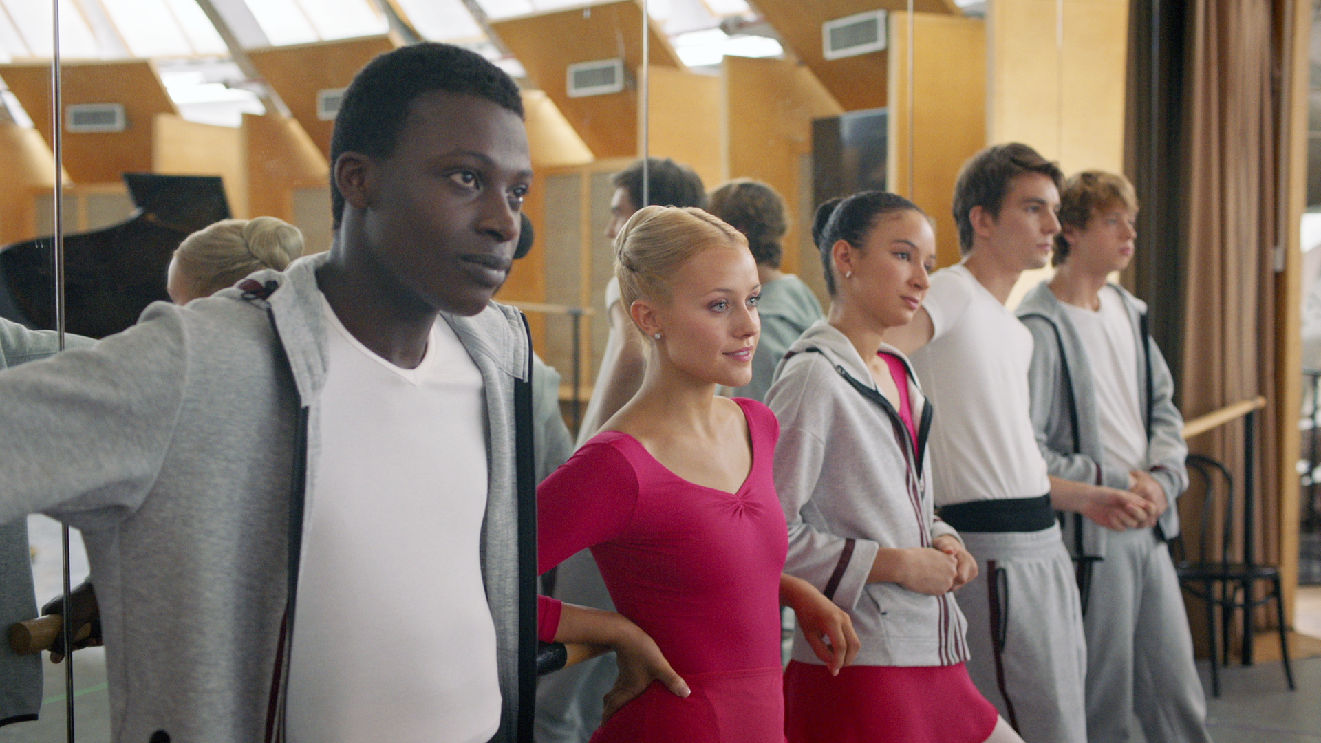 Isaac, Lena, Ines, Max und Jeff (v.l.n.r.) lehnen gemeinsam an der Ballettstange im Unterrichtsraum der Balettschule. Die Wand hinter ihnen ist verspiegelt.