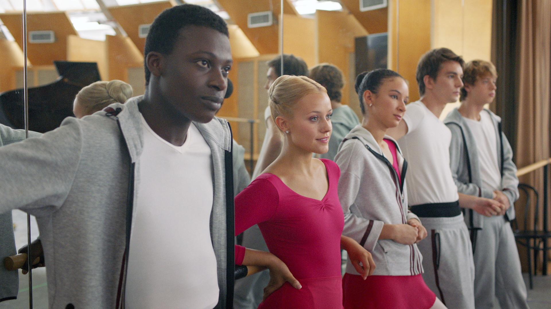 Isaac, Lena, Ines, Max und Jeff lehnen gemeinsam an der Ballettstange im Unterrichtsraum der Balettschule. Die Wand hinter ihnen ist verspiegelt.