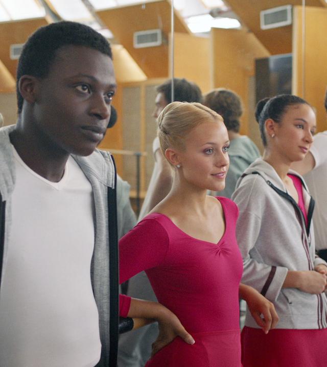 Isaac, Lena, Ines, Max und Jeff lehnen gemeinsam an der Ballettstange im Unterrichtsraum der Balettschule. Die Wand hinter ihnen ist verspiegelt.