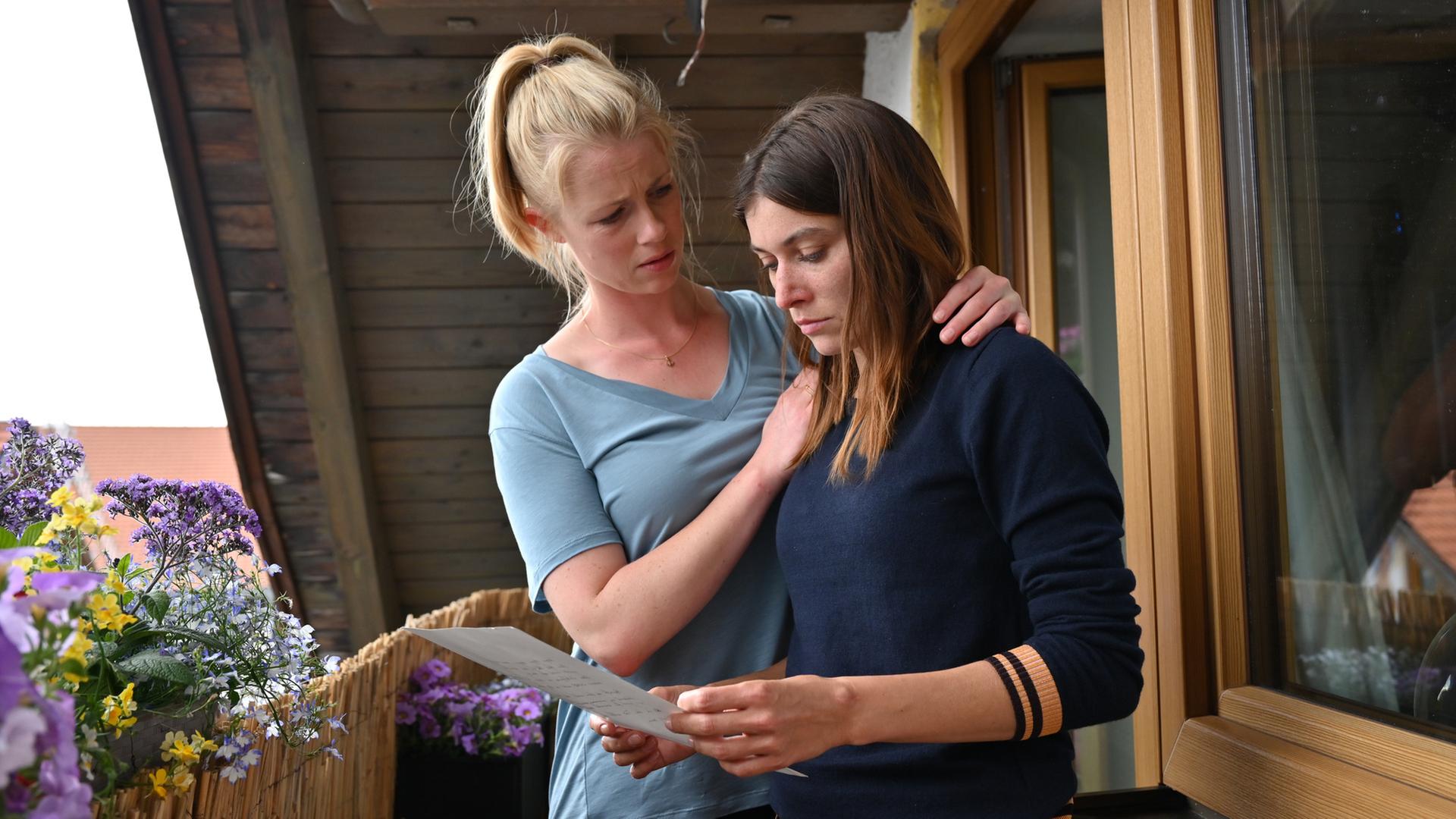 "Marie fängt Feuer - Alles oder Nichts": Angie (Sylta Fee Wegmann) steht mit einem Brief in der Hand auf ihrem Balkon. Marie (Christine Eixenberger) steht neben ihr und hat tröstend ihren Arm um Angies Schulter gelegt.