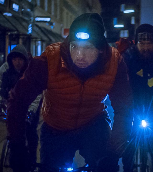 Eine Gruppe Radfahrer fährt auf einer dunklen Straße. Vorneweg Adam Berg (Eric Stehfest). Er trägt eine Kopfleuchte.