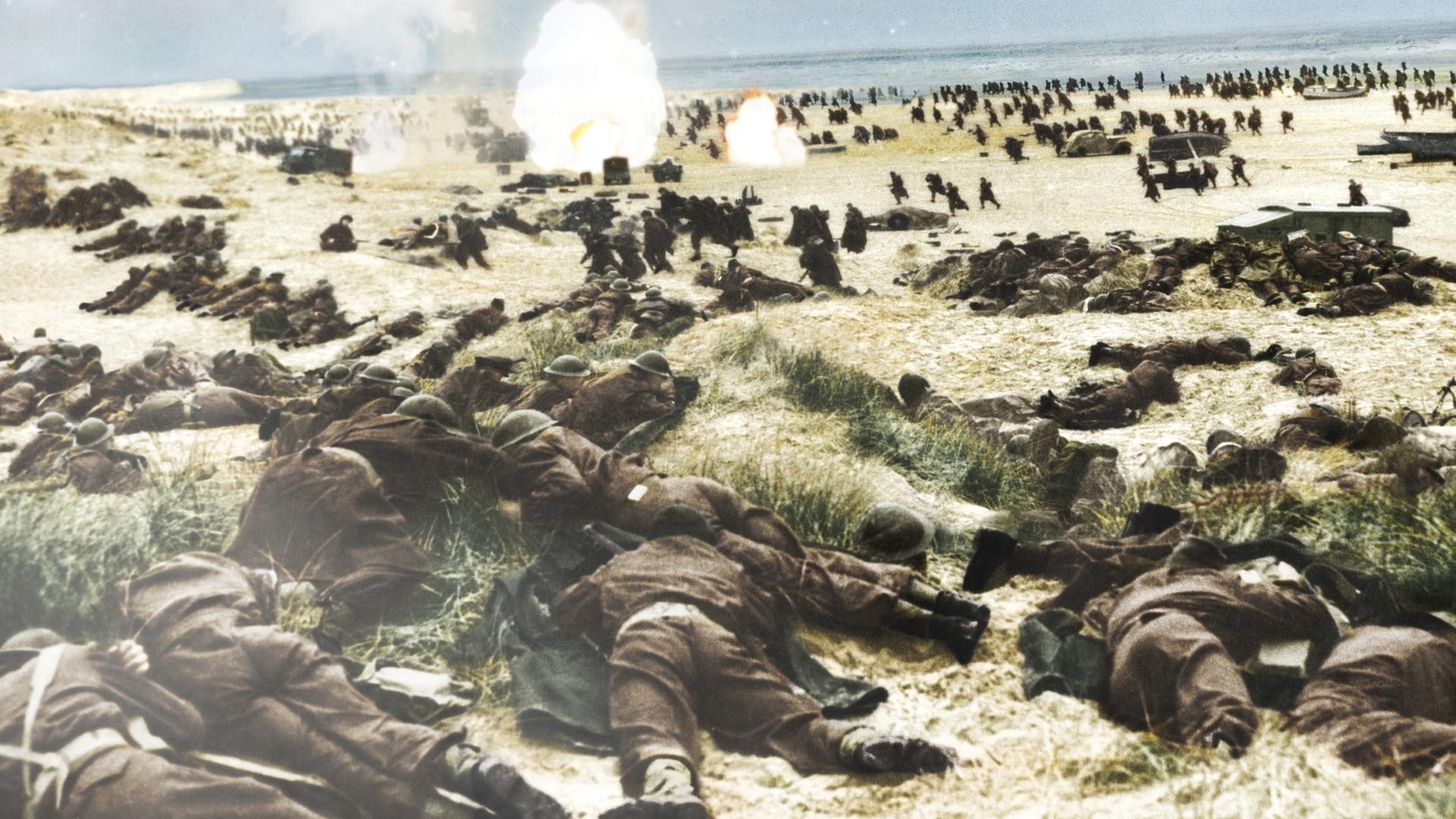 Alliierte Soldaten 1940 am Strand von Dünkirchen, versteckt in den Dünen und laufend am Strand. Im Hintergrund sind vereinzelte Explosionen zu erkennen. 