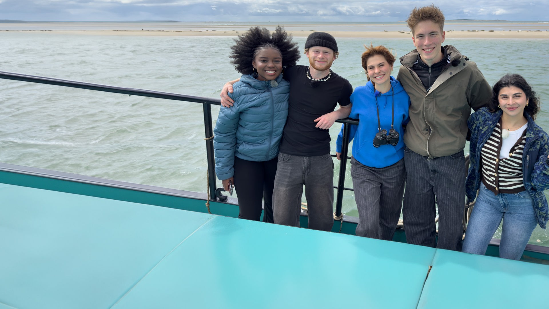 Jafait, Justus, Angelina, Rouven und Ella stehen auf einem Segelboot - im Hintergrund eine Sandbank mit Seehunden