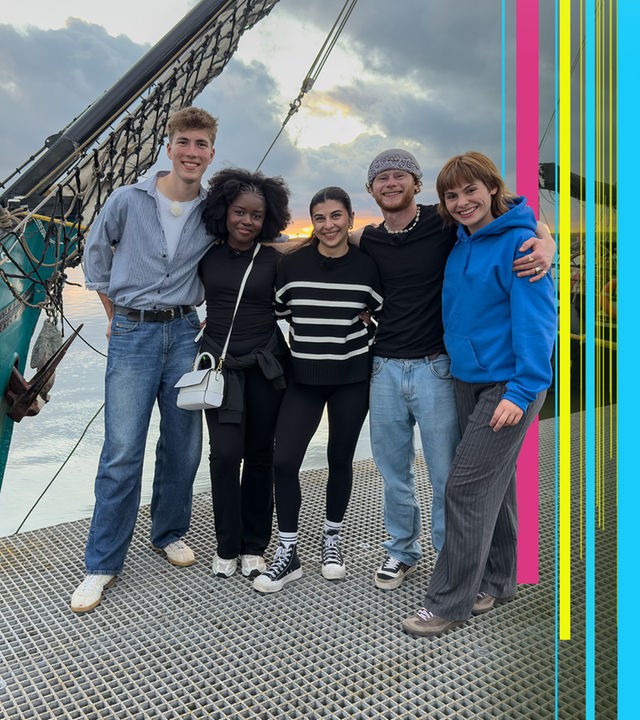 Rouven, Jafait, Ella, Justus und Angelina stehen im Hafen vor einem Segelschiff