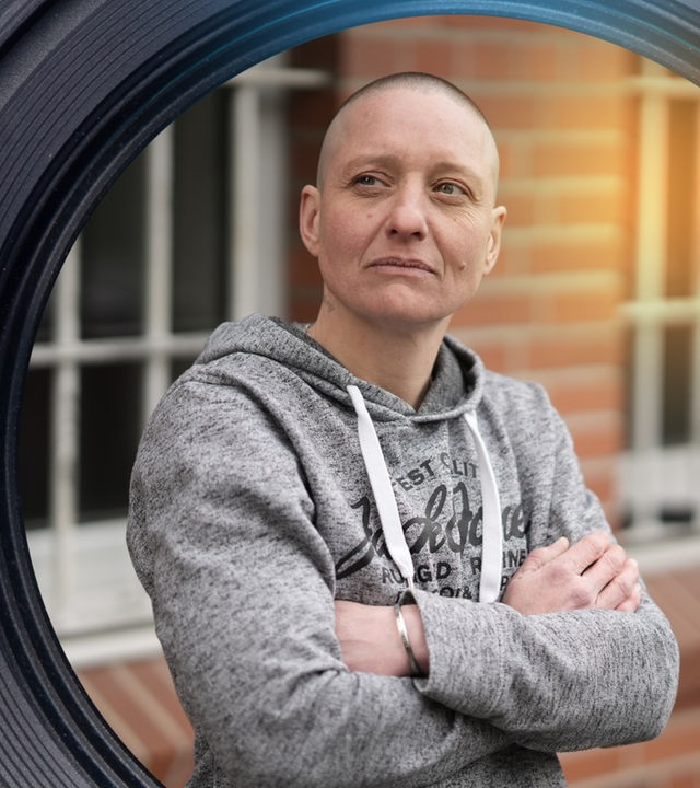 Eine Frau steht mit verschränkten Armen vor einem Gitterfenster.