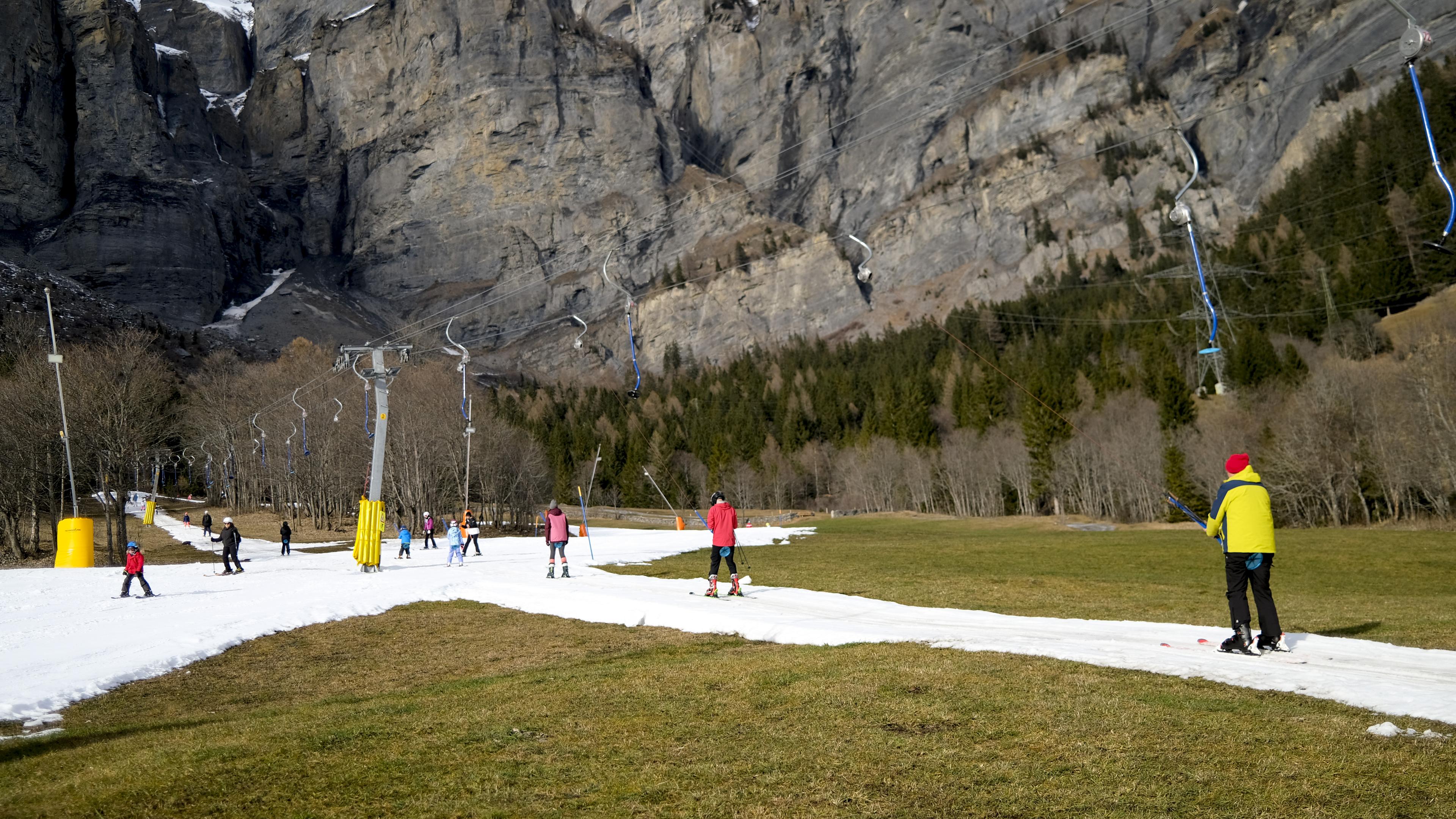Schweiz, Leukerbad: Skifahrer benutzen einen Lift auf einer künstlich beschneiten Skipiste inmitten eines schneefreien Feldes auf 1411 Metern über dem Meeresspiegel.