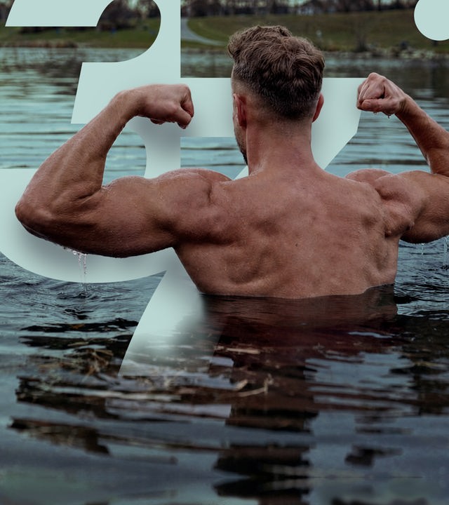 Ein Mann steht in der Donau mit dem Rücken der Kamera zugewandt. Das Wasser reicht bis unter die Achseln. Er beugt die Arme nach oben und macht Fäuste. Er präsentiert seinen muskulösen Oberkörper.