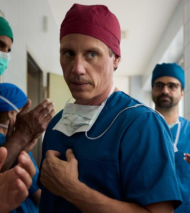  Im Flur der Klinik läuft Dr. Nice (Patrick Kalupa) an seinen applaudierenden Mitarbeitern vorbei. Dr. Schmidtke (Maximilian Grill) läuft etwas abseits hinter ihm her und beobachtet dies missmutig.