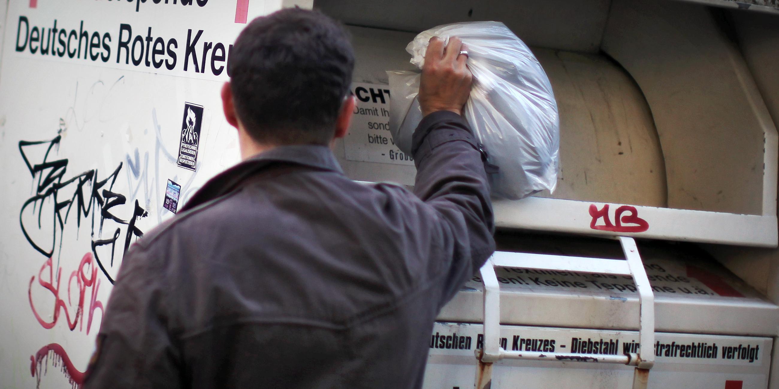 Ein Mann wirft einen Beutel in einen Altkleider-Container des Deutschen Roten Kreuzes.