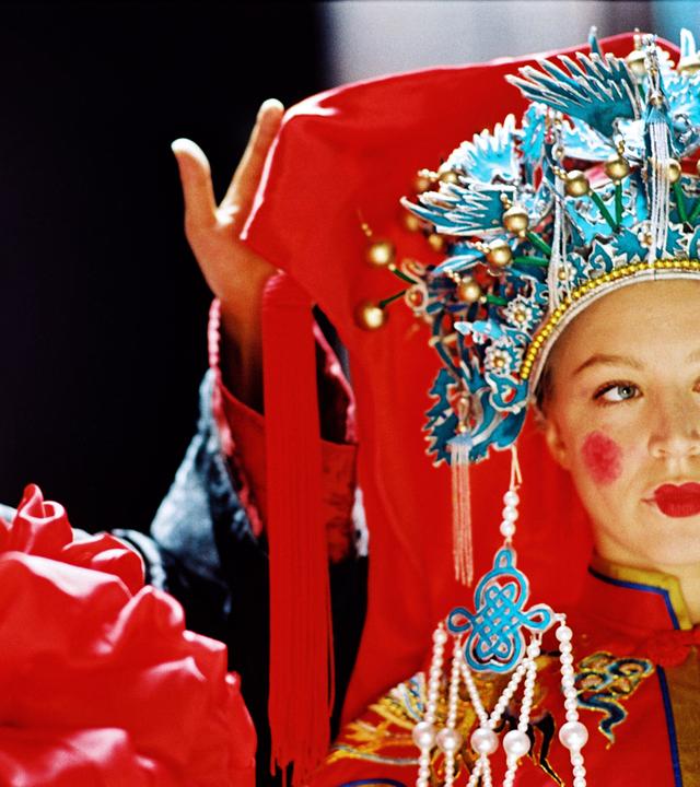 Eine junge Frau in aufwendigem, traditionell chinesischem Brautgewand mit perlenbesetztem Kopfschmuck steht neben einem lächelnden Mann in festlicher Kleidung