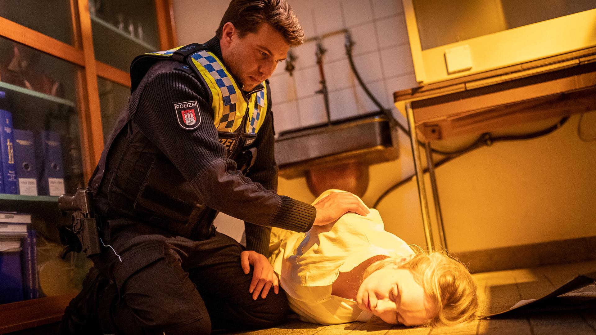 "Notruf Hafenkante - Am Ende der Lüge": Der Polizist Nick Brandt (Raúl Richter) sitzt in der Hocke neben Sandra Mertens (Katharina Heyer). Sie liegt in einem Kellerraum auf dem Boden. Ihre Augen sind geschlossen. Nick rüttelt an ihrer Schulter.