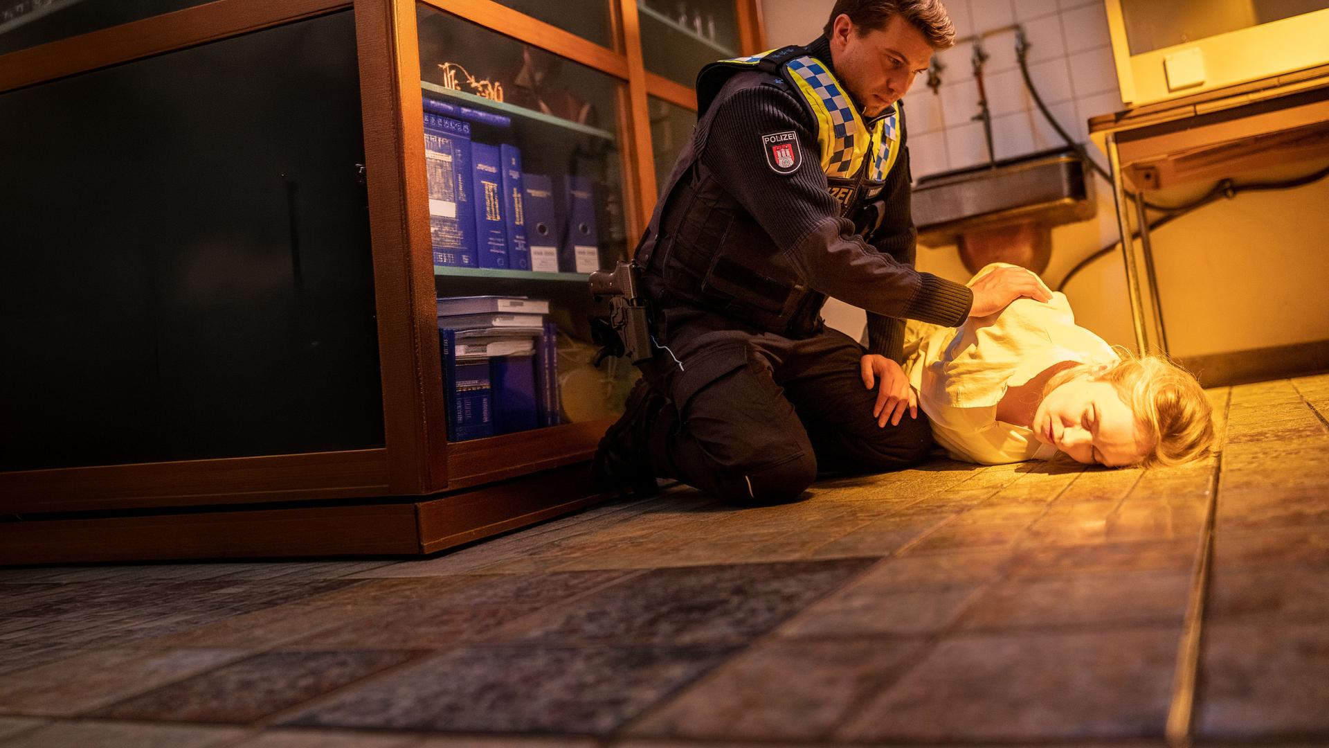 "Notruf Hafenkante - Am Ende der Lüge": Der Polizist Nick Brandt (Raúl Richter) sitzt in der Hocke neben Sandra Mertens (Katharina Heyer). Sie liegt in einem Kellerraum auf dem Boden. Ihre Augen sind geschlossen. Nick rüttelt an ihrer Schulter.