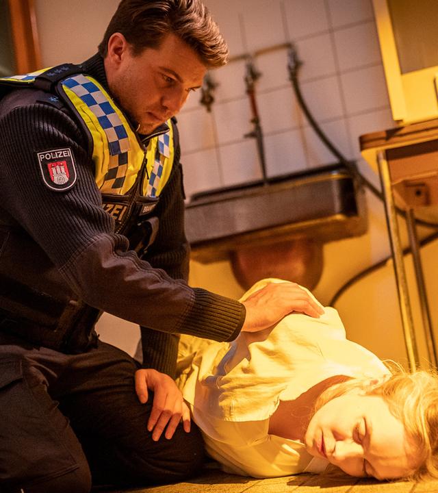 "Notruf Hafenkante - Am Ende der Lüge": Der Polizist Nick Brandt (Raúl Richter) sitzt in der Hocke neben Sandra Mertens (Katharina Heyer). Sie liegt in einem Kellerraum auf dem Boden. Ihre Augen sind geschlossen. Nick rüttelt an ihrer Schulter.