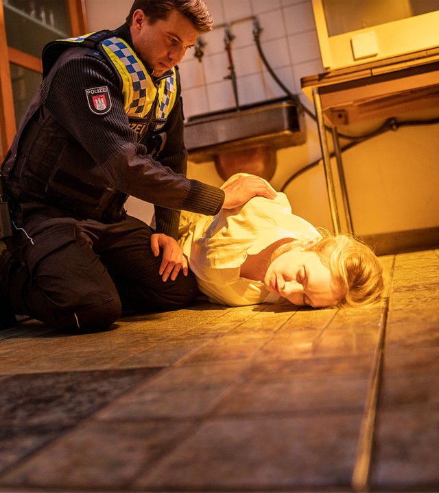 "Notruf Hafenkante - Am Ende der Lüge": Der Polizist Nick Brandt (Raúl Richter) sitzt in der Hocke neben Sandra Mertens (Katharina Heyer). Sie liegt in einem Kellerraum auf dem Boden. Ihre Augen sind geschlossen. Nick rüttelt an ihrer Schulter.