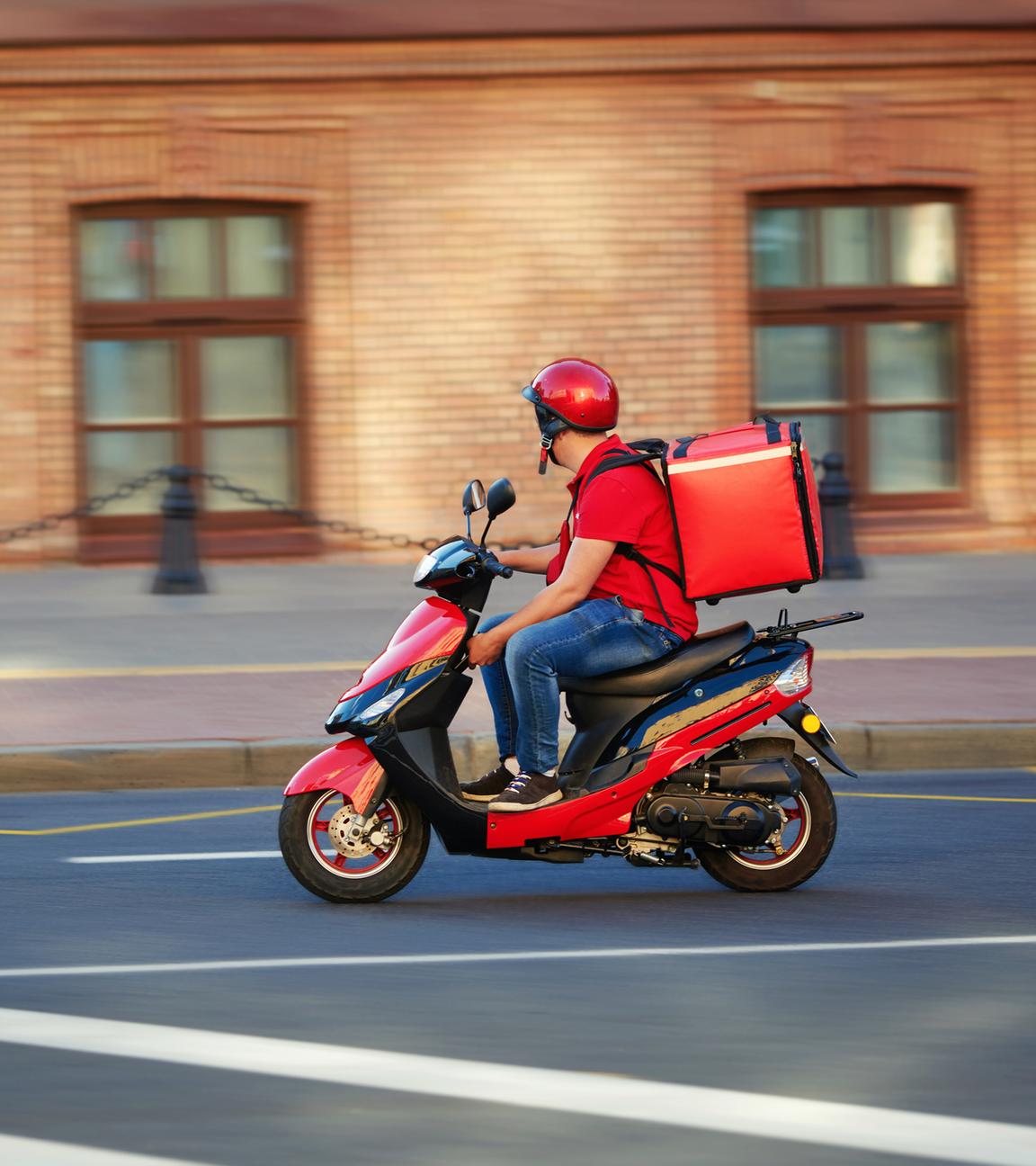 Ein Lieferdienstfahrer fährt mit seinem Moped und seiner roten Tragetasche auf dem Rücken durch die Straßen.
