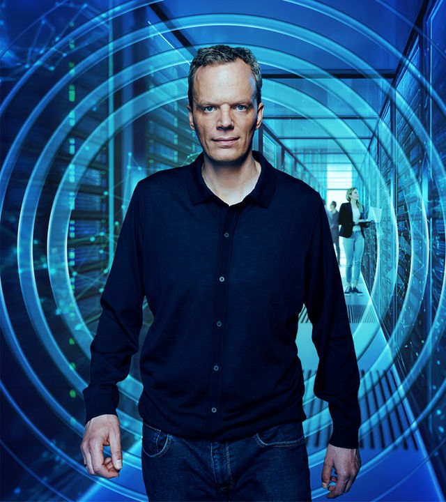 ZDF-Wirtschaftsexperte Florian Neuhann kommt auf den Betrachter zu, während im Hintergrund Menschen an Servern arbeiten