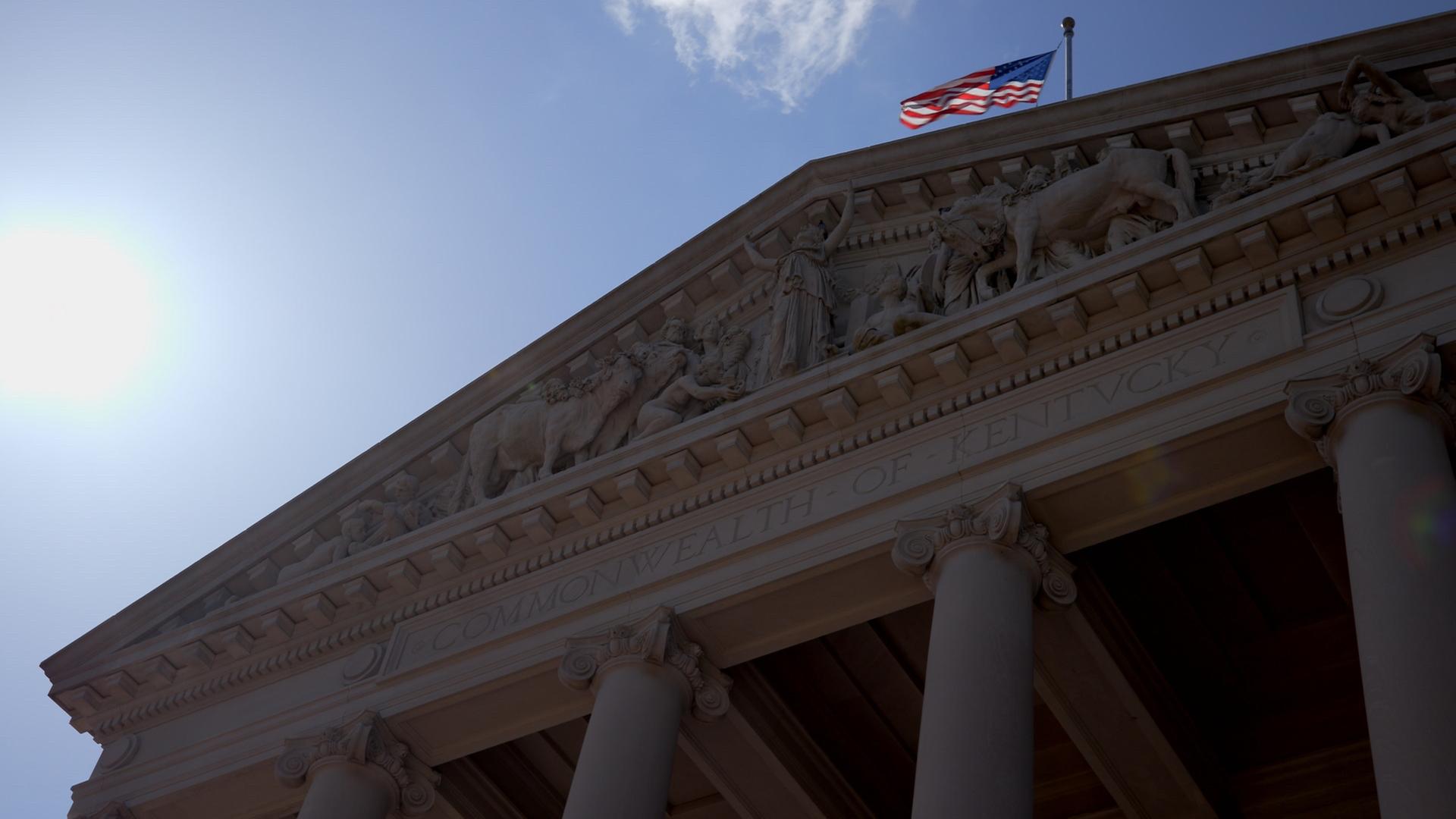 "Amerikas verzockte Renten - Vom Staatsdienst in die Armut": Froschperspektive auf die Säulenhalle des Kentucky State Capitol mit im Wind flatternder US-amerikanischer Flagge auf der Spitze.