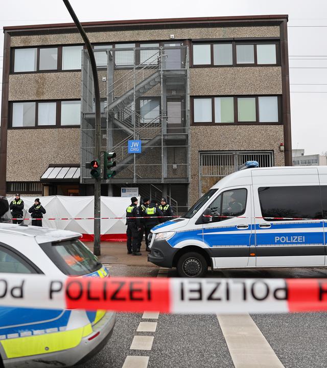 Im Mittelpunkt des Bildes ist ein Auto der Hamburger Polizei zu sehen; im Vordergrund verschwommen ein rot-weißes Absperrband.