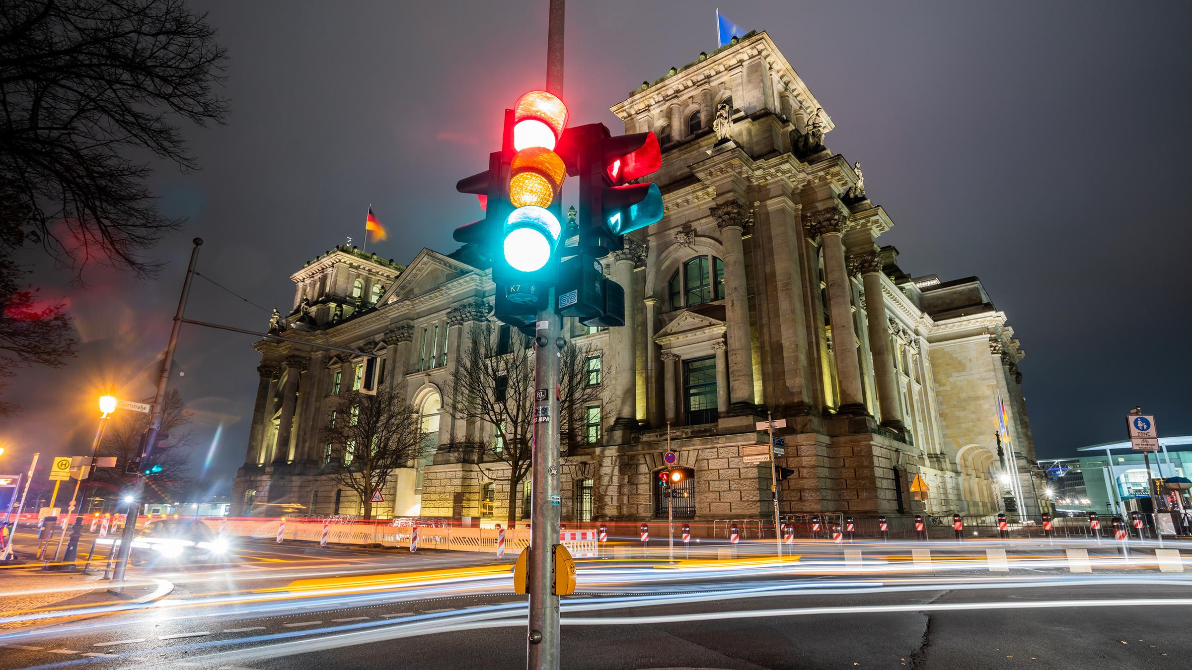 Eine Ampel leuchtet in einer Aufnahme mit Langzeitbelichtung am Morgen vor dem Reichstagsgebäude