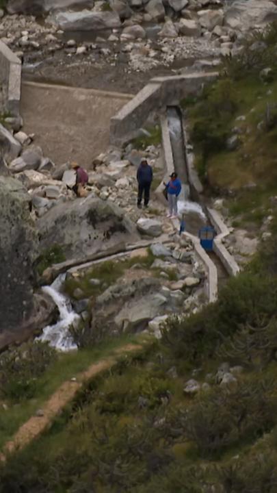 Zwei Menschen von oben, sie stehen in einem steinigen Tal, duch das Bewässerungskanäle laufen, die "Amunas".