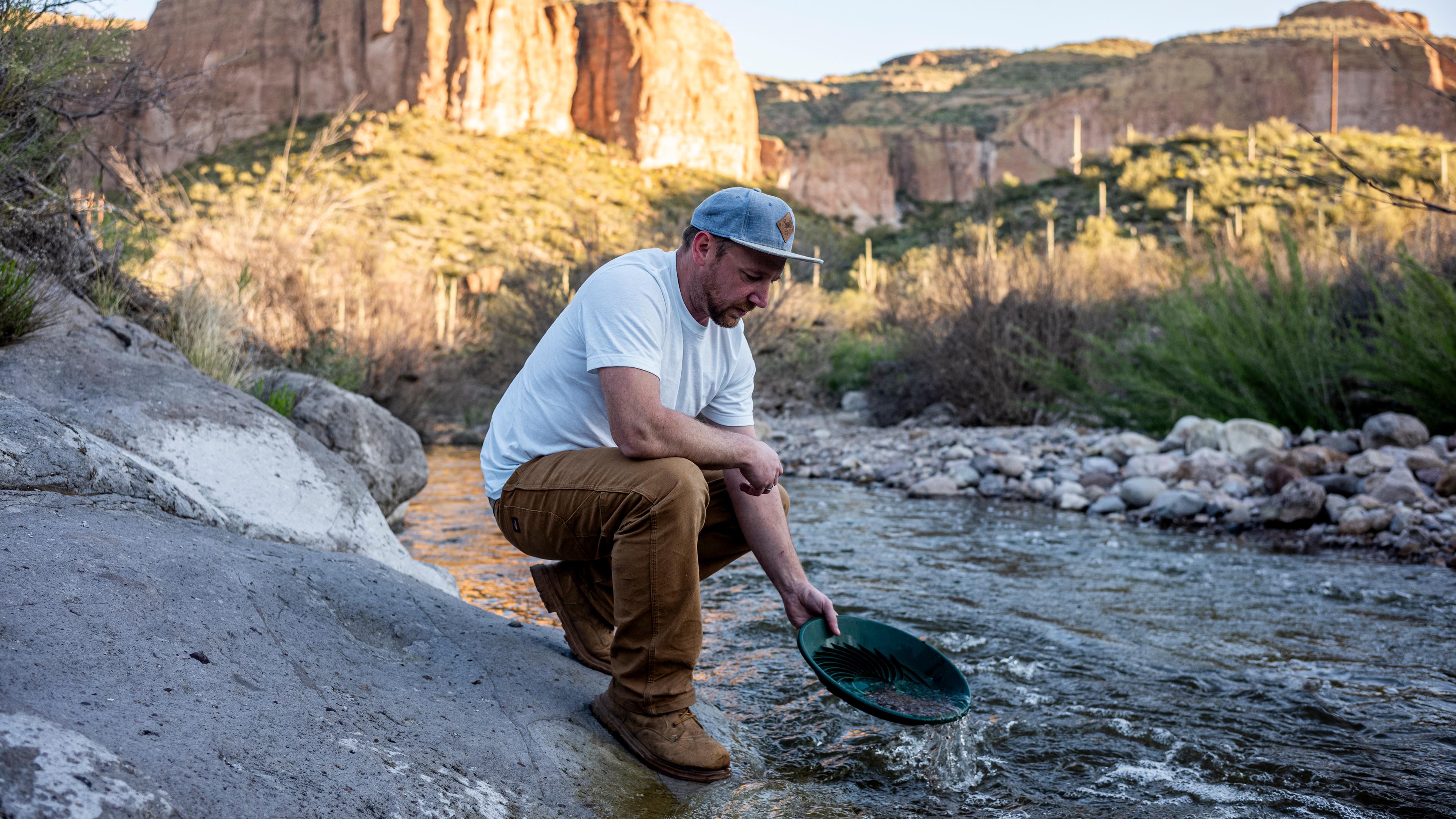 André wäscht Gold am Ufer eines Flusses. Im Hintergrund sind große rötliche Felswände.